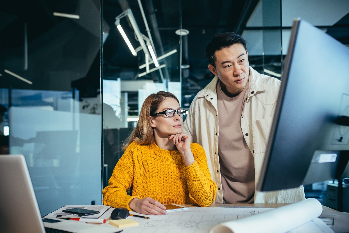 Two freelancers, an Asian man and a woman, work in a modern office, discussing and discussing a joint project, looking at a computer monitor-1