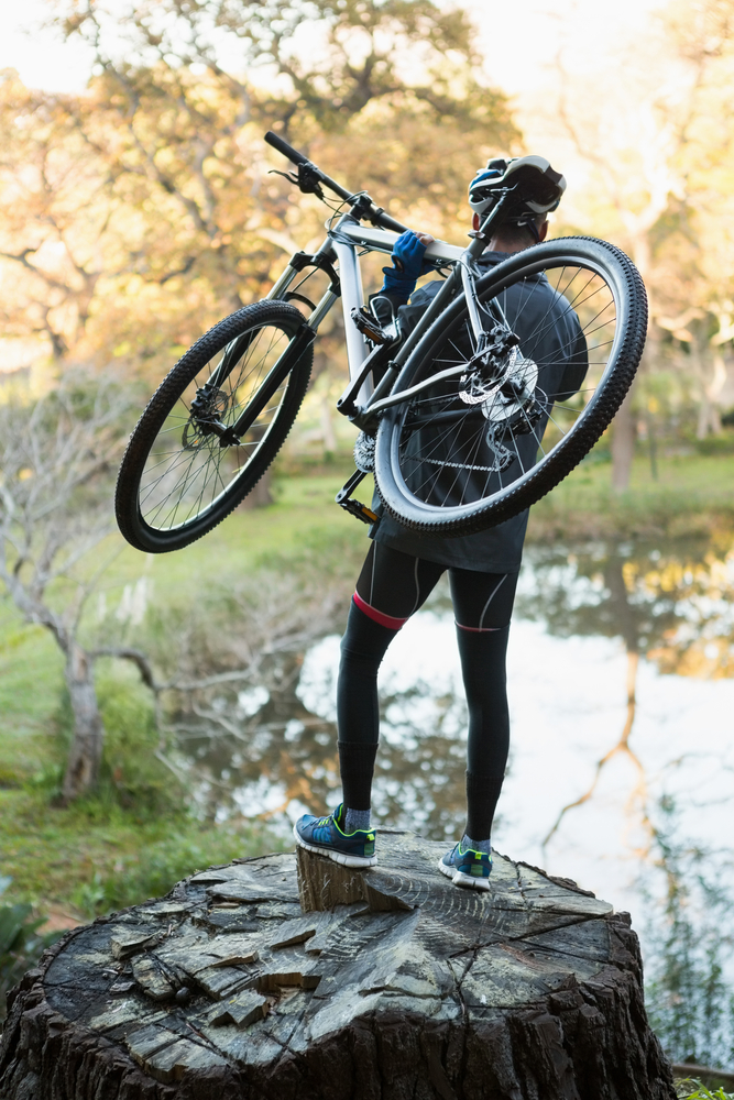 Male mountain biker carrying bicycle looking at nature in the forest